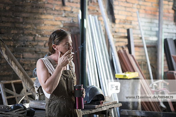 Female welder in metal workshop taking a break  smoking cigarette