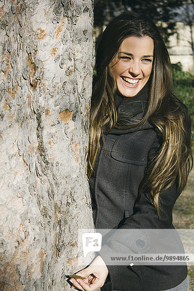 Spanien  Madrid  Porträt der lachenden Frau  die sich am Baumstamm lehnt