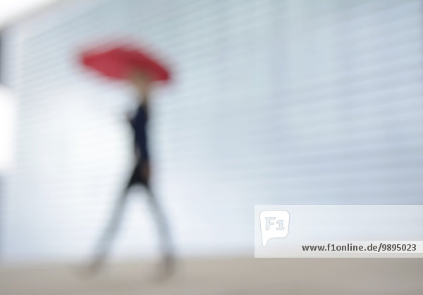 Geschäftsfrau läuft mit rotem Regenschirm