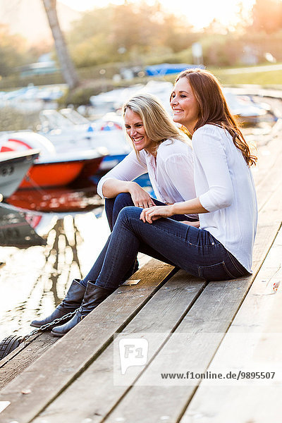 Zwei lachende Frauen sitzen auf der Strandpromenade.