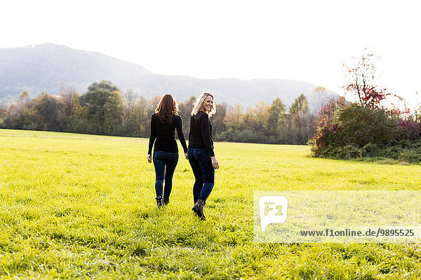 Lesbian couple walking hand in hand on a meadow