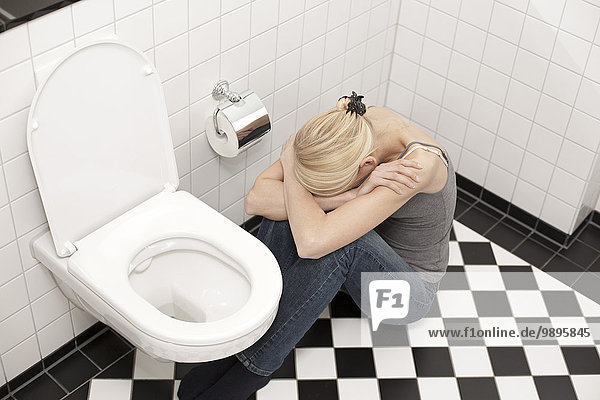Verzweifelte magersüchtige junge Frau auf der Toilette