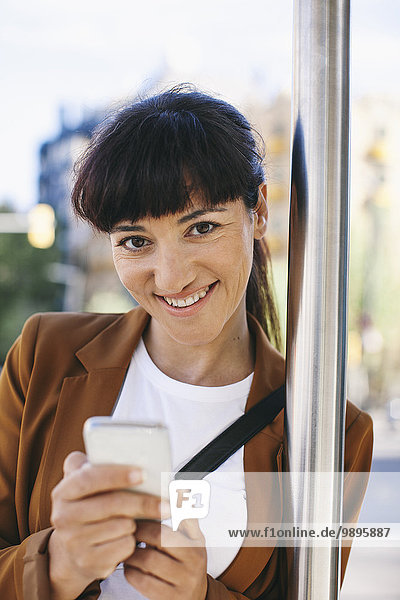 Porträt einer lächelnden Geschäftsfrau mit Smartphone an der Bushaltestelle