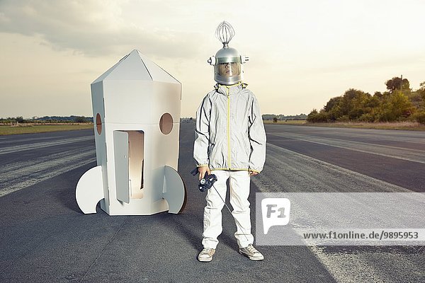 Junge verkleidet als Raumfahrer an der Papprakete stehend