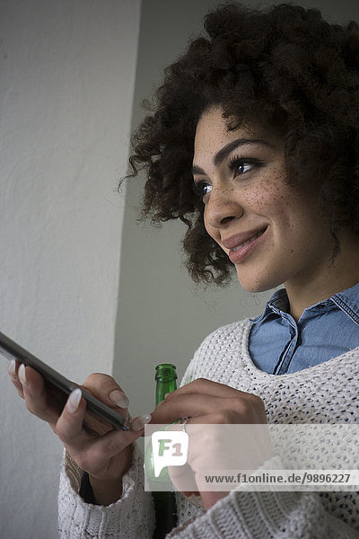 Smiling young woman holding beer bottle and smartphone