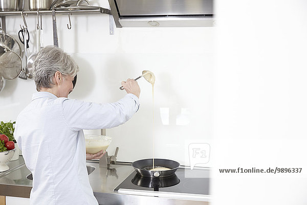 Mature woman in kitchen preparing pancakes