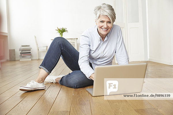 Reife Frau auf dem Boden sitzend mit Laptop