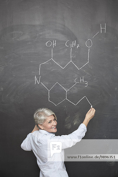 Reife Lehrerin beim Zeichnen der chemischen Formel an der Tafel