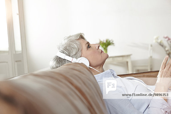 Reife Frau sitzt auf der Couch und hört Musik.