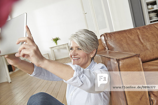 Reife Frau zu Hause  die Selfie mit digitalem Tablett nimmt