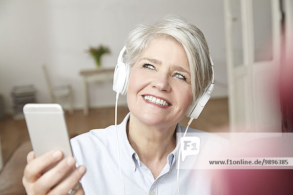 Mature woman holding smartphone and wearing headphones