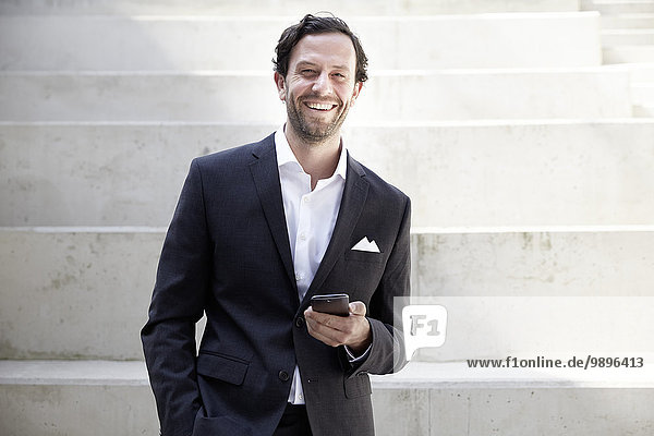 Lächelnder Geschäftsmann mit Smartphone in einem modernen Gebäude