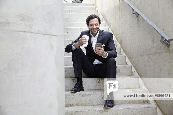 Geschäftsmann mit Kaffee zum Mitnehmen mit Smartphone in einem modernen Gebäude