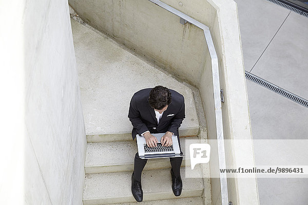 Geschäftsmann auf der Treppe eines modernen Gebäudes sitzend mit Laptop