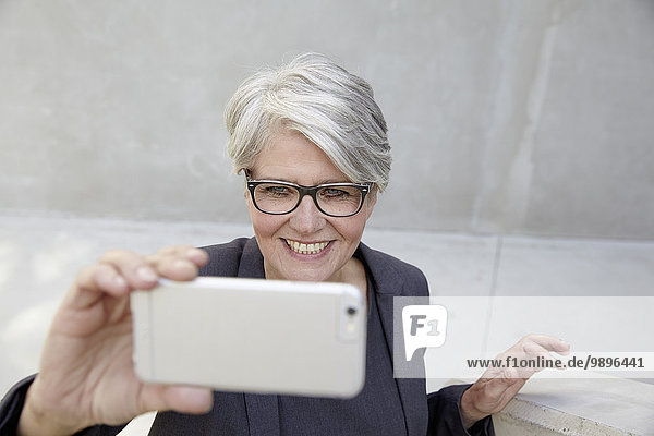 Porträt einer lächelnden Karrierefrau  die einen Selfie mit dem Smartphone nimmt.
