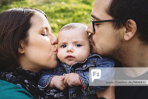 Mother and father kissing baby outdoors