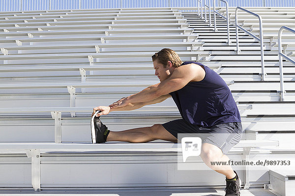 USA  California  San Luis Obispo  young man doing stretching exercises on a grandstand