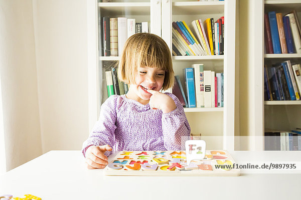 Porträt eines lächelnden kleinen Mädchens  das das Alphabet mit Holzbuchstaben lernt.
