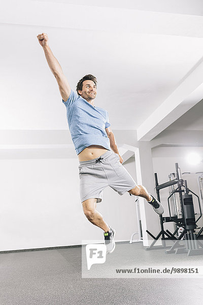 Junger Mann  der im Fitnessstudio in die Luft springt.