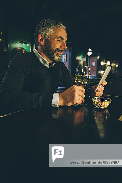 Smiling man sitting at counter of a pub using smartphone