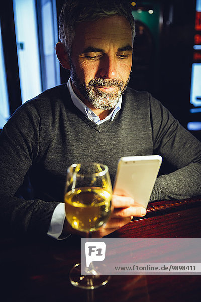 Portrait of man sitting at counter of a pub using smartphone