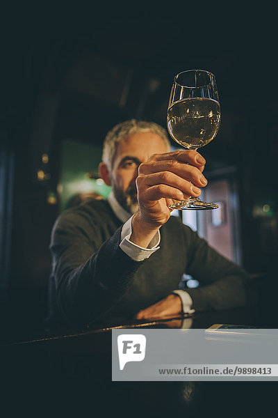 Man sitting at counter of a pub watching white wine glass