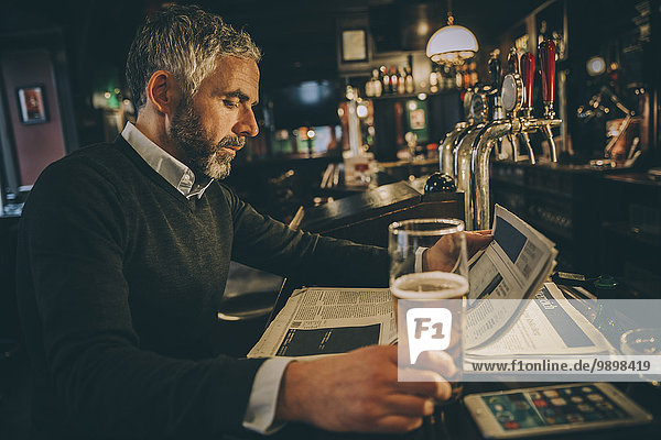 Man sitting at counter of a pub reading newspaper