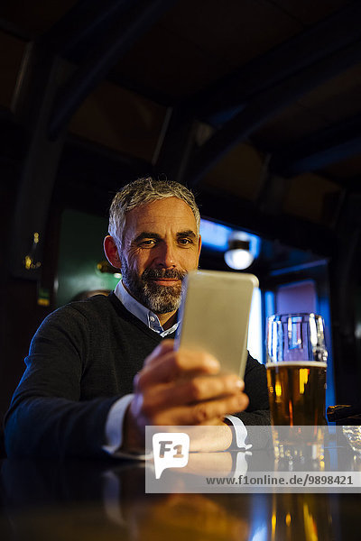 Man sitting at counter of a pub looking at his smartphone