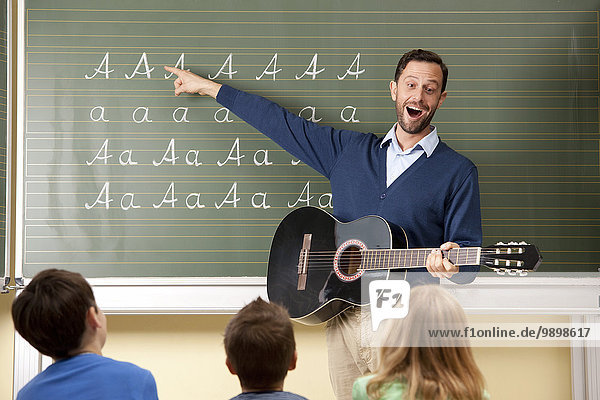 Lehrer mit Gitarre an der Tafel mit Variationen des Buchstabens A