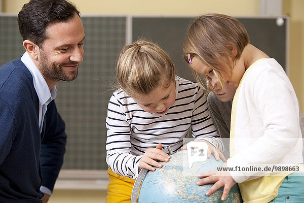 Teacher and pupils looking at globe in classroom