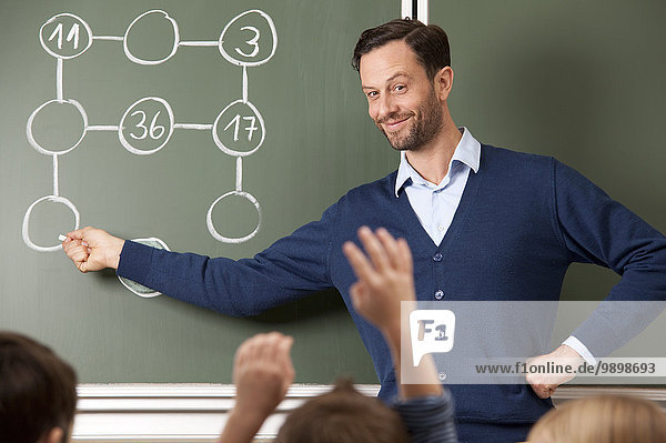 Lächelnder Lehrer an der Tafel mit Rechenaufgabe