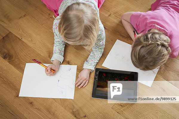 Zwei Schwestern mit digitalem Tablett und Papierbögen auf dem Boden