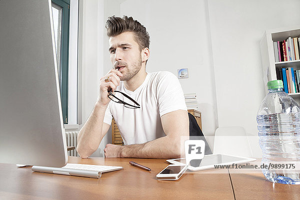 Nachdenklicher junger Mann sitzt am Schreibtisch in einem Büro