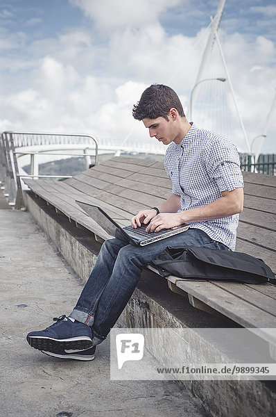 Spain  Ferrol  young man using a laptop outdoors