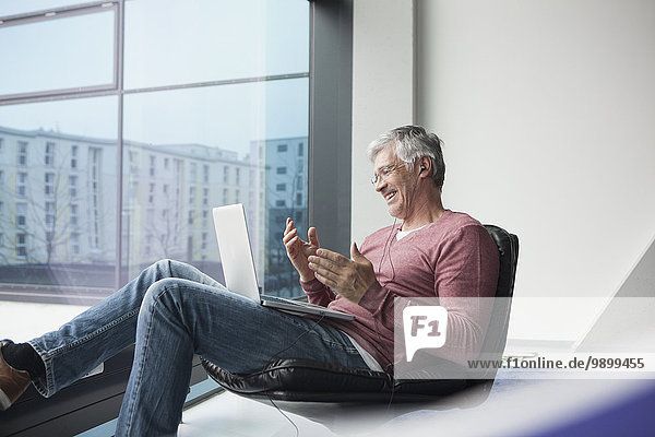 Mann sitzend in einem Ledersessel skyping mit Laptop