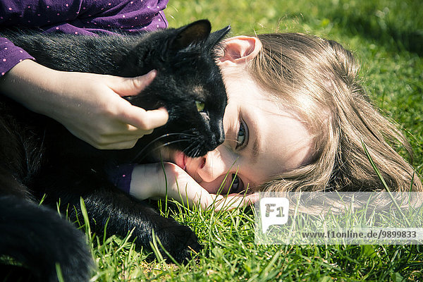 Mädchen auf einer Wiese liegend mit schwarzer Katze