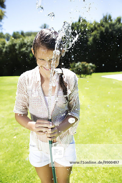Junges Mädchen spritzt Wasser mit Gartenschlauch