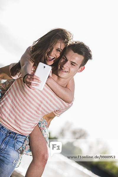 Verspieltes junges Paar mit Selfie im Freien