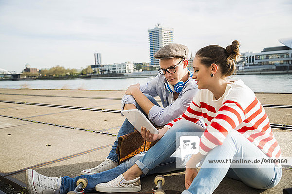 Junger Mann und Frau auf Schienen sitzend mit digitalem Tablett