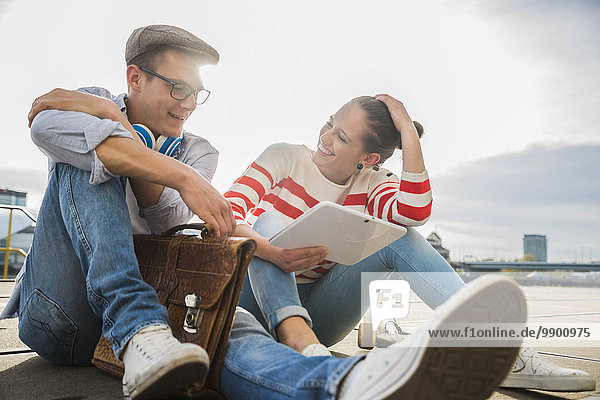 Junger Mann und Frau auf dem Boden sitzend mit digitalem Tablett