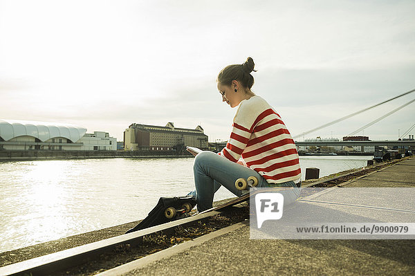 Junge Frau sitzend am Flussufer mit digitalem Tablett