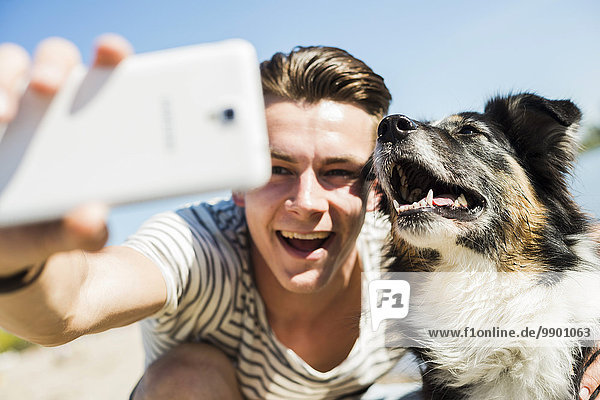 Fröhlicher junger Mann nimmt Selfie mit Hund mit ins Freie