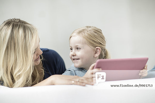 Mutter und kleine Tochter auf Couch mit digitalem Tablett