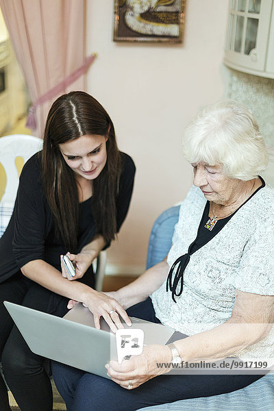 Grandmother and granddaughter using laptop together at home
