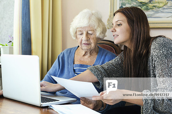 Großmutter und Enkelin mit Dokument mit Laptop zu Hause