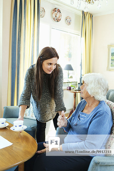 Young woman serving coffee to grandmother at home