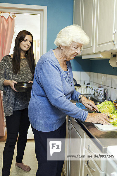 Junge Frau sieht Großmutter bei der Zubereitung des Essens in der Küche zu.