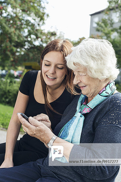 Young woman looking at grandmother using smart phone at park