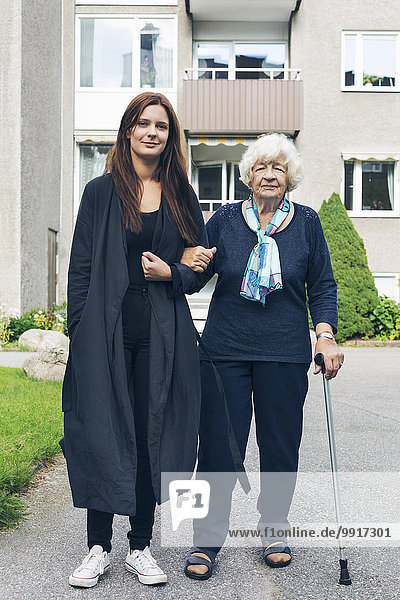 Ganzflächiges Porträt einer jungen Frau mit Großmutter vor dem Haus