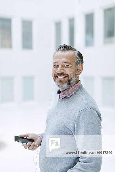 Porträt eines glücklichen Geschäftsmannes  der Musik über ein Smartphone im Büro hört.